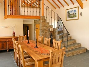 Un coin repas avec une table et des chaises en bois, un escalier en pierre et un tableau accroché au mur.