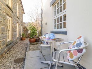 Ein Steinhaus mit einer kleinen Terrasse, ausgestattet mit einem Metalltisch und Stühlen, Blumentöpfen und einem Fenster.