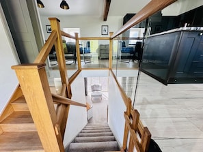 Una escalera de madera con barandas de vidrio que lleva a una habitación con vistas a un comedor.