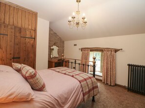 Ein Schlafzimmer mit Bett, Holzschrank, einer Deckenleuchte, einem Fenster mit Vorhängen und einem Heizkörper.