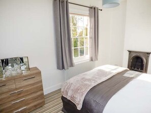 Ein Schlafzimmer mit Bett, Schminktisch, Fenster mit Vorhängen und Kamin.