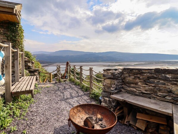 A rustic outdoor seating area with a stone wall, a wooden bench, and a fire pit. - Pengarreg in Barmouth, Gwynedd (Barmouth)