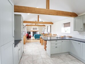 A kitchen with a central island, wooden beams, light-colored cabinets, and a dining area with chairs and a sofa. - The Piggery nr Abergele, Conwy (Abergele)