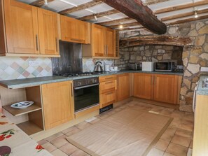 A kitchen with wooden cabinets, a stone wall, a tiled backsplash, and a microwave. - The Cottage: Idyllic Views Await (Llangollen)