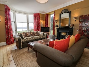 A living room with a sofa, armchair, fireplace, and large windows. - Auchenvhin in Dalbeattie, 5bed (Dalbeattie)