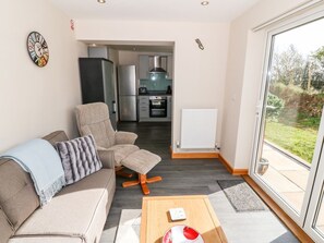 A modern living room with a sofa, a coffee table, and a view of a kitchen and outdoor area. - Min-y-rhos, Edern, North Wales (Pwllheli)