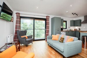 A modern living room with a sofa, armchair, and a dining area with a kitchen in the background. - 26 Strathtay Lodges, Aberfeldy (Aberfeldy)