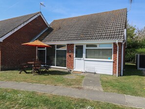 A residential house with a tiled roof, a brick exterior, a garage door, and a patio with a table and chairs. - 1 Kessingland Cottages, Kessingland (Lowestoft)