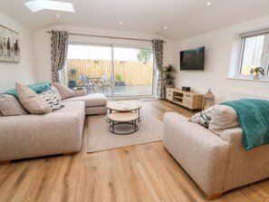 Ein modernes Wohnzimmer mit zwei Sofas, einem Couchtisch, einem Fernseher und einer Glastür zum Patio.