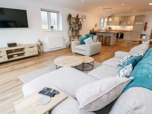 Ein modernes Wohnzimmer mit Sofa, Couchtisch und Fernseher. Im Hintergrund ist eine Küche zu sehen.