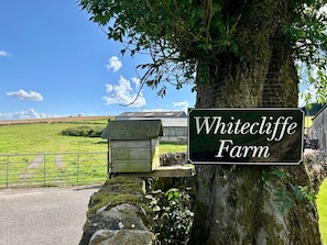 Schild für Whitecliffe Farm mit einer Steinmauer, einem Baum und einem grünen Feld im Hintergrund.