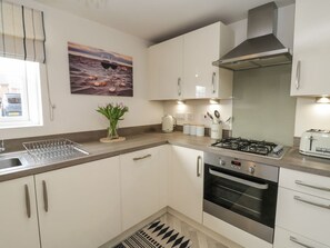 A modern kitchen with white cabinets, a gas stove, an oven, and a window with a view of the street. - Woodside View, Whitby (Whitby)