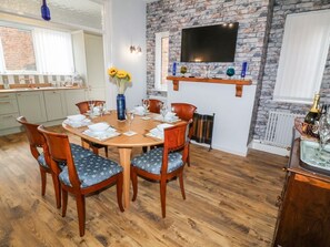 A dining area with a brick wall, a mounted TV, and a wooden dining table set for four. - 6 Canal Road, Ripon, North Yorkshire. (Ripon)