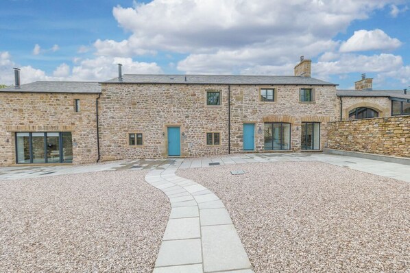 A stone building with a gravel courtyard, a curved pathway, and a blue door.