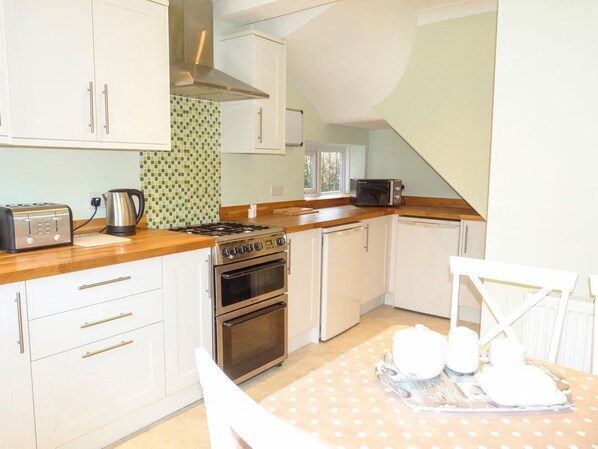 A kitchen with white cabinets, a stove, a toaster, and a microwave. - Amelia Cottage, Battle (Battle)