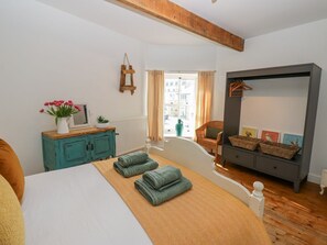 A bedroom with a bed, a dresser, a chair, a hanging rack, and a view of the outside.