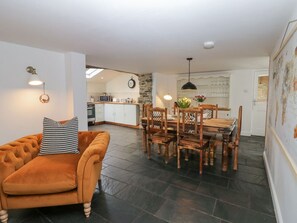 A cozy living room with a sofa, a dining table with chairs, a kitchen in the background, and a staircase leading upstairs.