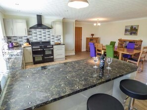 A modern kitchen with a central island, built-in oven, and a dining area with a table and chairs. - Bryn Tirion, Betws Yn Rhos (Abergele)