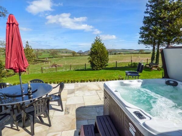 A hot tub with a view of a grassy field, a table with chairs, and a red umbrella. - Bryn Tirion, Betws Yn Rhos (Abergele)