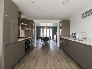 A modern kitchen with stainless steel appliances, a dining area with a table and chairs, and a view into the living room. - 21 Skippers Way, Walton-On-The-Naze (Walton on the Naze)