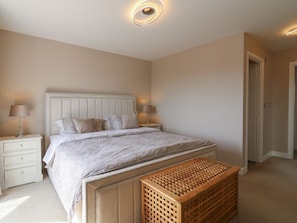 Een slaapkamer met een bed, nachtkastjes, een houten bankje en een deur.