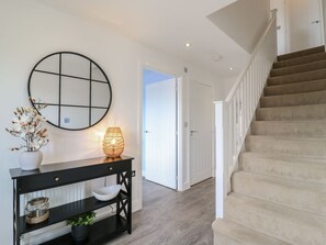 A staircase leading to a landing, a round mirror on the wall, a console table with decorative items, and a door in the background. - 21 Skippers Way, Walton-On-The-Naze (Walton on the Naze)