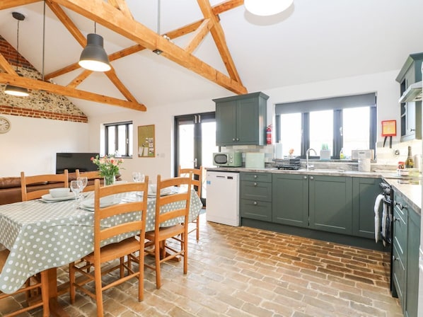 A kitchen with wooden beams, a dining table set for four, and a green cabinet.