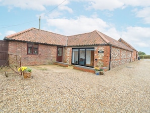 A brick building with a tiled roof, a gravel driveway, and a small garden area with potted plants.