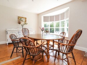 A dining area with a round table surrounded by wooden chairs, a white cabinet with blue accents, and a large window with a view of greenery. - Homewood, Garstang, Lancashire (Preston)