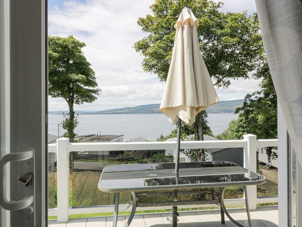 A balcony with a table and an umbrella, overlooking a body of water and trees.