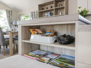 A kitchen area with a wooden shelf, a white appliance, snacks, a black trash bag, and travel magazines. - Olivia's Haven, in Wemyss Bay. (Wemyss Bay)