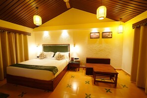 A hotel room with a bed, bedside table, lamp, and a wooden bench. - Anaasa Resorts  (Tiruvannamalai)