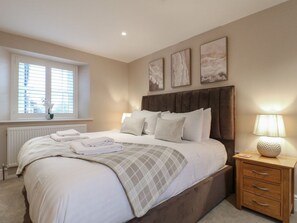 A bedroom with a large bed, a bedside table with a lamp, and a window with blinds. - The Coach House, Holloway (Matlock)
