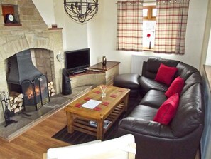 A living room with a fireplace, a leather sofa, a wooden coffee table, and a television.