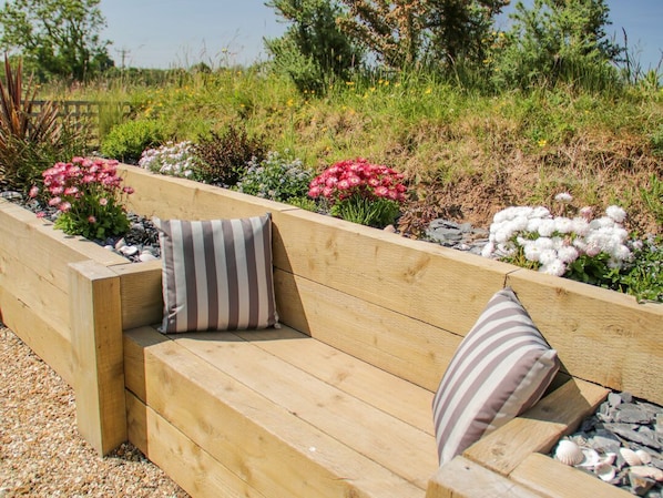 A wooden bench with striped cushions in a garden setting with various plants and flowers.