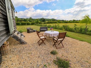 A gravel patio with a round table and four chairs, a wicker basket, and a small plant. - Goose Whistle Hut is in Foxham (Chippenham)