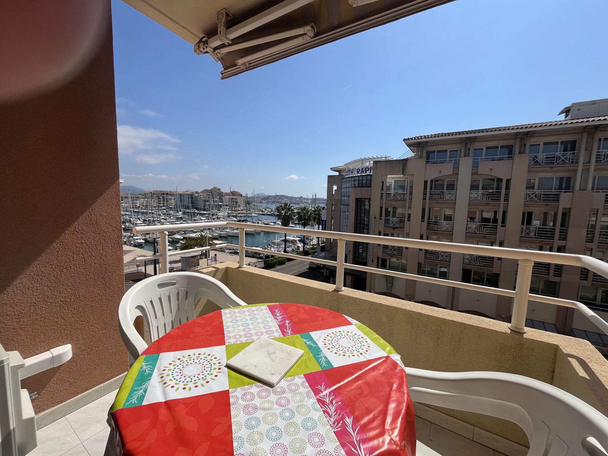 A balcony with a table and chairs, overlooking a marina and buildings.