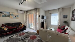 Ein Wohnzimmer mit Sofa, Couchtisch, Fernseher und einer Glasschiebetür, die auf einen Balkon führt.