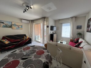 Ein Wohnzimmer mit Sofa, Couchtisch, Fernseher und einer Glasschiebetür, die auf einen Balkon führt.