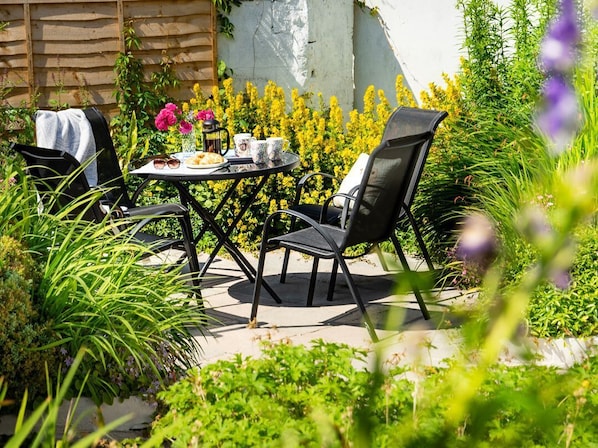 An outdoor patio with a round table, two chairs, and a small table with cups and a plate.