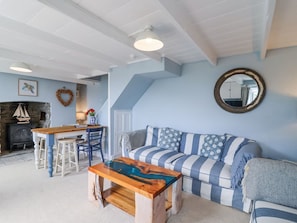 A cozy living room with a sofa, a coffee table, a fireplace, and a dining area. - 2 Cliff Cottages, Gorran Haven (Truro)