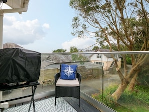 Ein Balkon mit Grill, ein Sessel mit Kissen und Blick auf eine Wohngegend mit Bäumen und Häusern.