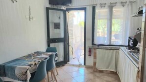 Ein Zimmer mit Esstisch, Stühlen, einer Küchenzeile und einer Glasschiebetür, die zu einem Außenbereich führt.