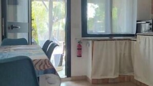 Ein Zimmer mit Esstisch, Stühlen, einer Küchenzeile und einem Fenster mit Vorhängen.