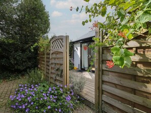 Ein hölzernes Tor führt zu einem Haus mit einer kleinen Veranda und einem Holzzaun.