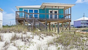 A beach house with a wooden deck, a balcony, and a large window. - Adorable and affordable gulf front, large 2 bedroom, 2 bath beach home. Salty Heir has so much to offer! (Gulf Shores)