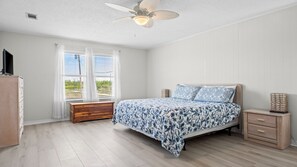 Une chambre à coucher avec un lit, une commode en bois, une table de chevet et un ventilateur de plafond.