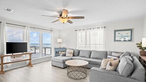 A living room with a large gray sectional sofa, a round coffee table, a ceiling fan, and a TV on a stand. - Adorable and affordable gulf front, large 2 bedroom, 2 bath beach home. Salty Heir has so much to offer! (Gulf Shores)