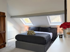 A bedroom with a bed, skylights, a nightstand, a bedside table, and a vase with red flowers. - Cottage, Lytham St. Annes (Lytham St. Annes)