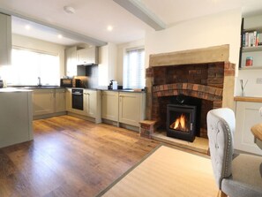 A modern kitchen with a fireplace, wooden flooring, and a dining area with a chair. - Cottage, Lytham St. Annes (Lytham St. Annes)